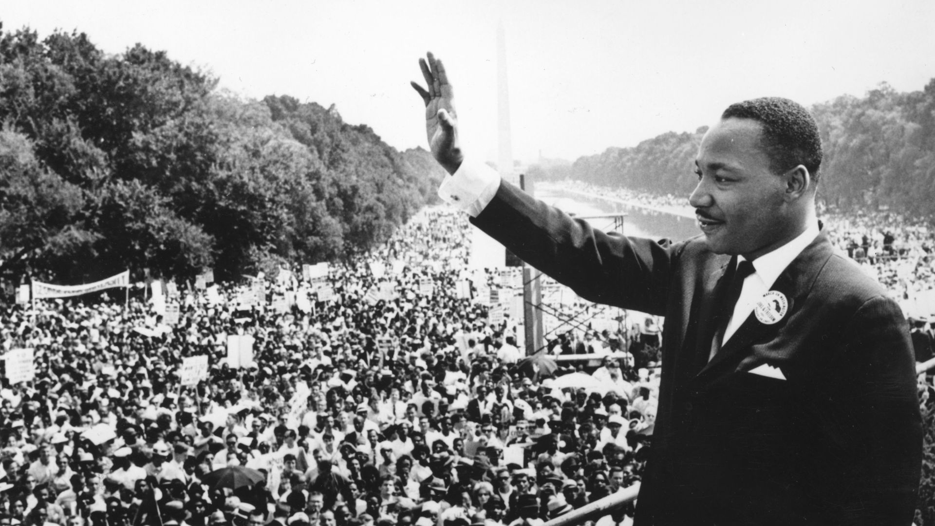 Martin Luther King, Jr. In A Suit Raising His Hand In Front Of A Large Crowd